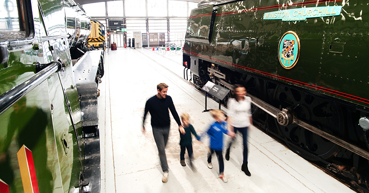 family walking past trains and engines inside Locomotion museum